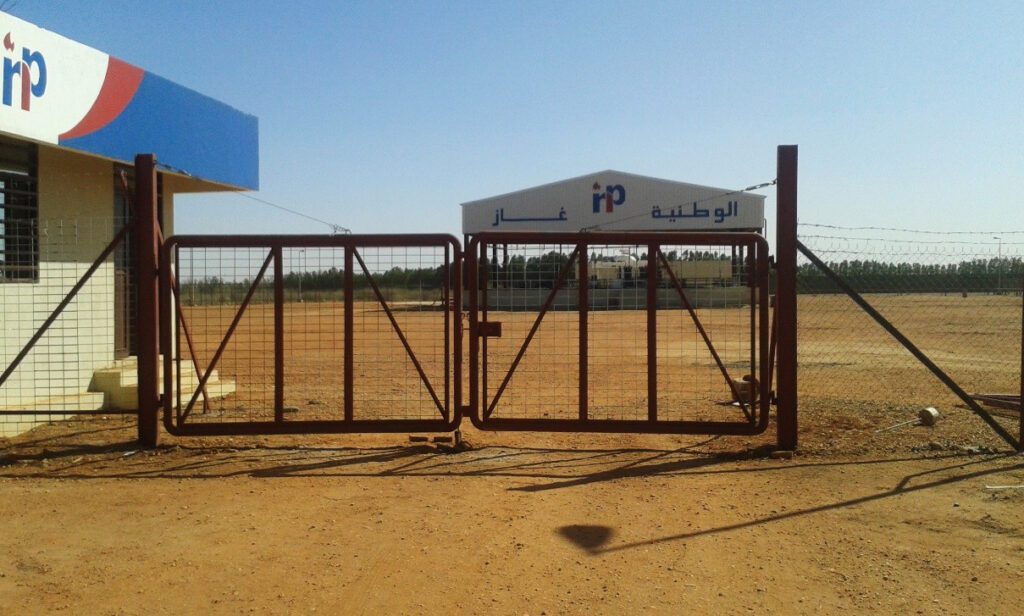 An external view showing the main security gate of the new gas warehouse, with the main filling center and loading platforms under a metal roof equipped with safety systems in the background.