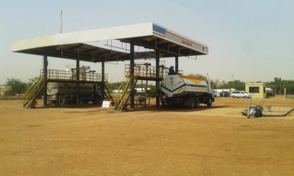 A land loading platform equipped with overhead filling arms, on which tanker trucks appear during refueling operations, designed to ensure the speed and efficiency of distributing petroleum derivatives to service centers.