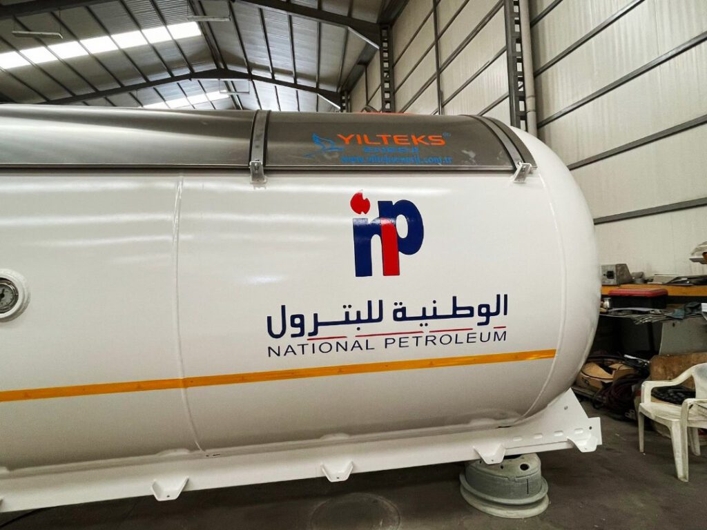 خزان صهريج غاز مسال قيد التصنيع أو الصيانة داخل ورشة فنية تخصصية، يبرز جودة اللحامات الهيكلية والطلاء المقاوم للتآكل، مع ظهور شعار الشركة والعلامات التعريفية الفنية.